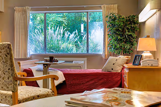 A senior living patient bedroom with a bed, window view, and seating area.