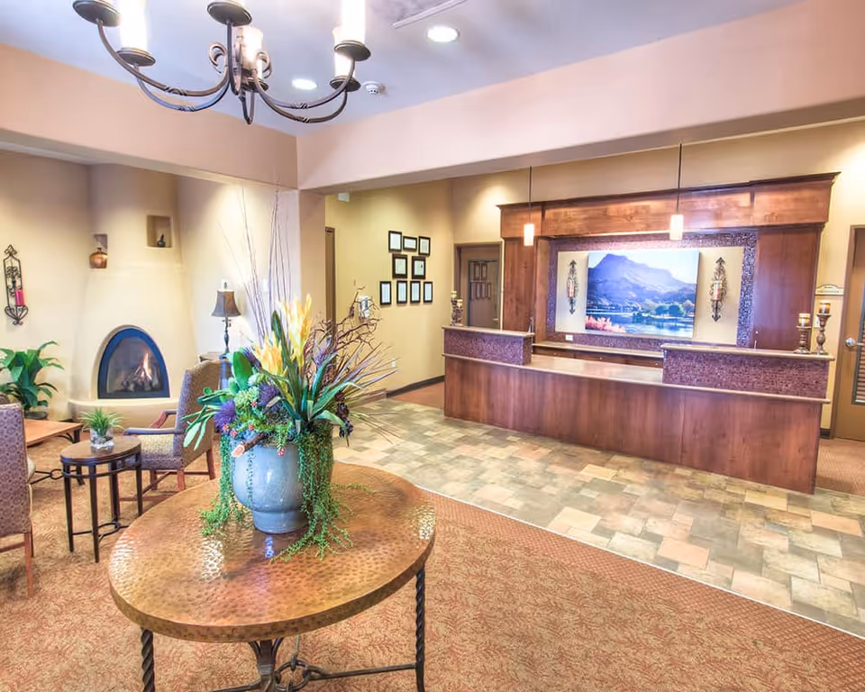 Reception lobby with a wooden front desk, seating area, fireplace, and a round table topped with a floral arrangement.