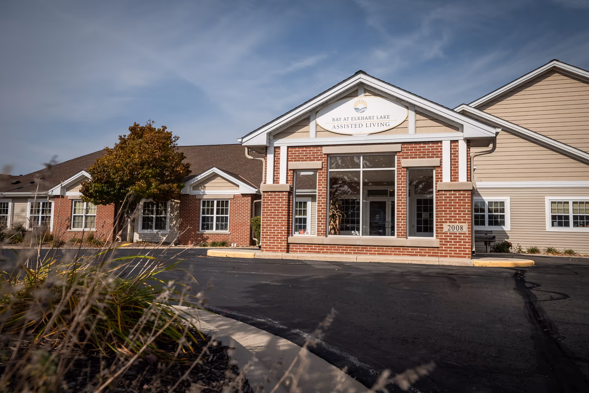 Front entrance of the Bay at Elkhart Lake assisted living building with a brick façade, large windows, and a driveway.