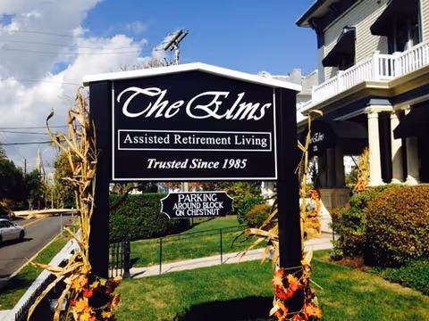 Front sign reads The Elms Assisted Retirement Living beside a two-story building.