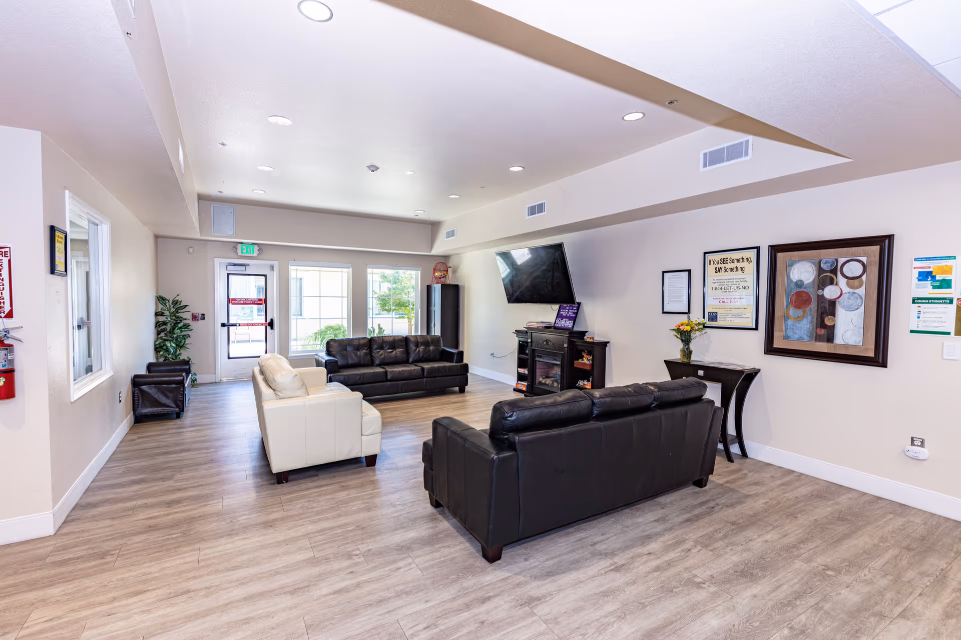 Bright senior living lounge with couches, a wall-mounted TV, and framed artwork.