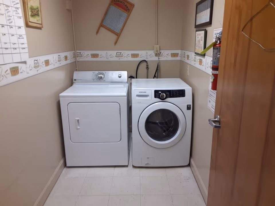 A small laundry room with a top-load dryer and front-loading Samsung washer side by side against beige walls.