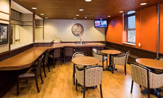 Small pub-style common room with a wooden bar, bar stools, round tables and chairs, a 'PUB' sign on the wall and a mounted TV.