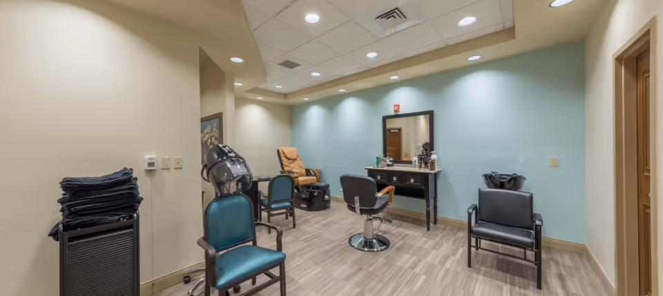 Interior salon room with styling chairs, a mirror, hair dryer stations, and stacked towels.