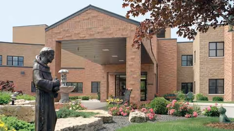 Exterior view of St Francis Terrace entrance with brick building, garden, and statue.