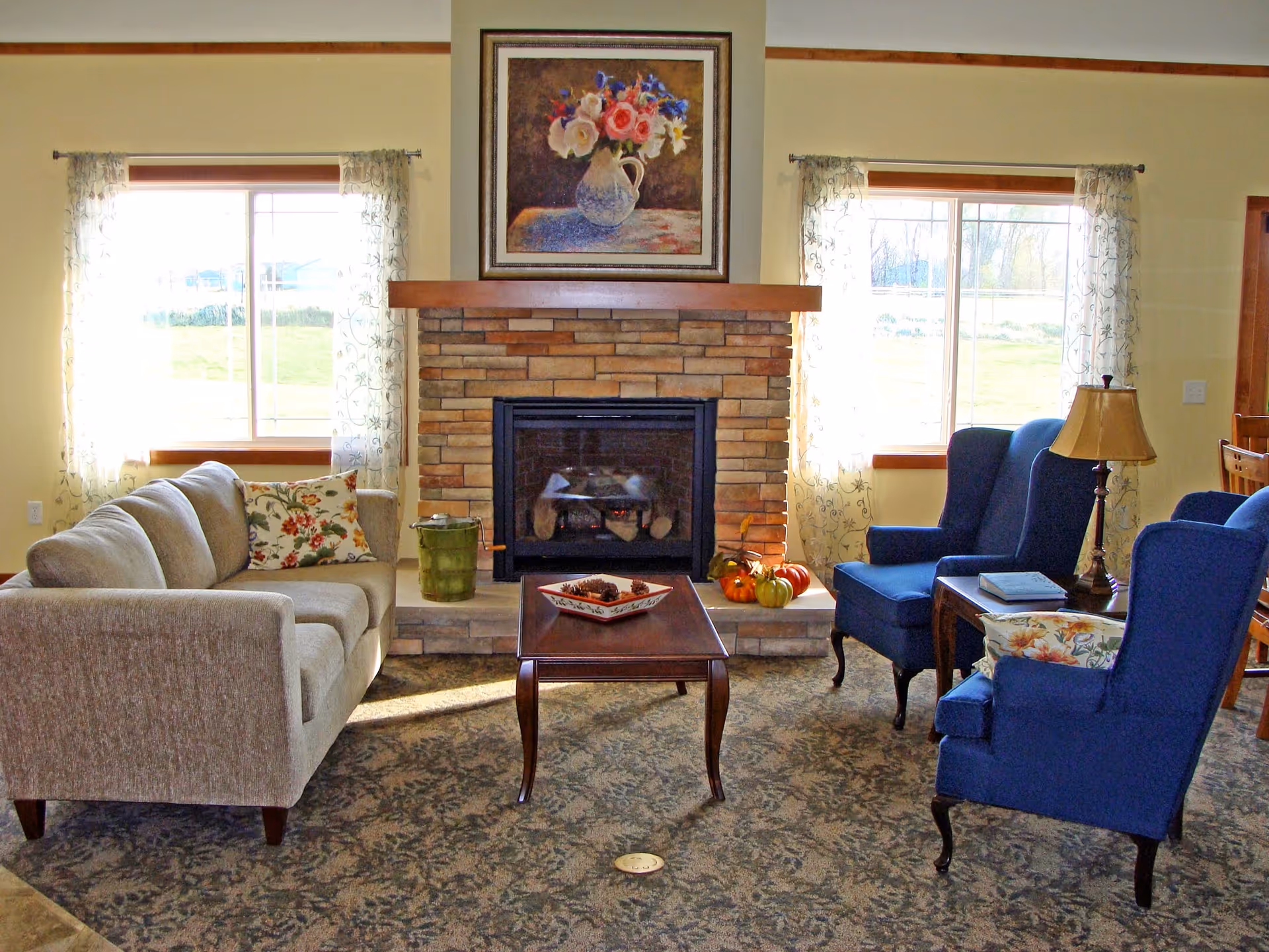Cozy living room with a stone fireplace between two windows, a gray sofa, two blue armchairs and a wooden coffee table.