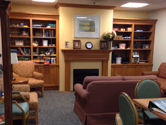 Cozy senior living lounge with a fireplace flanked by built-in bookshelves, sofas, and chairs.