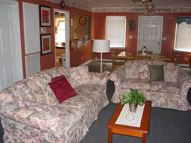 Cozy living room with floral sofas, a coffee table, and a dining area.