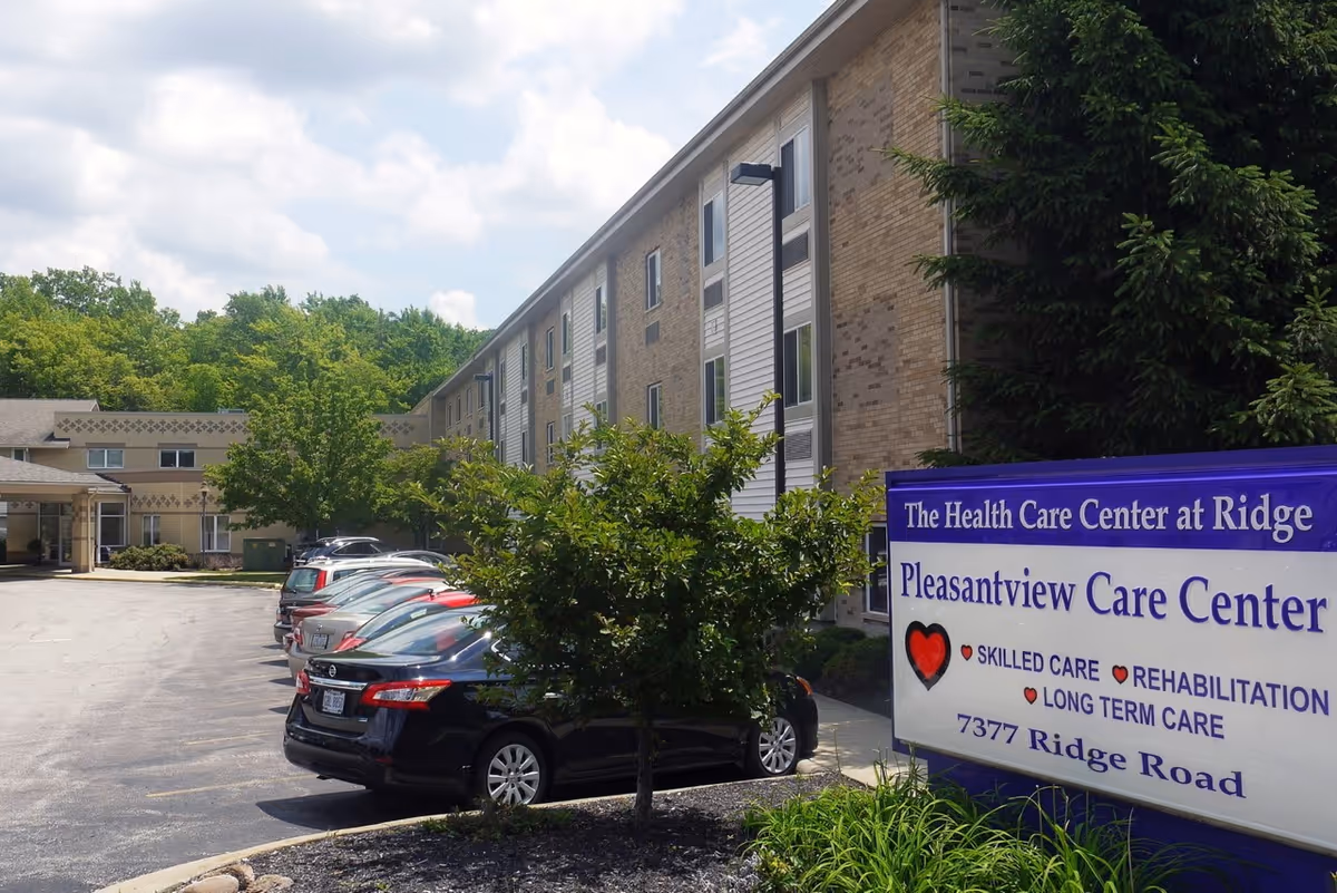 Exterior view of a brick senior care building with a blue sign and parked cars.