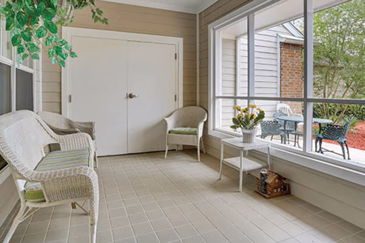 Sunroom with white wicker chairs and a small table with flowers overlooking an outdoor patio through large windows.