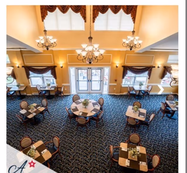 View from above of an elegant high-ceiling dining room with round and square tables, chandeliers, and patterned carpet.