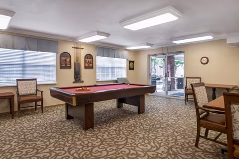 Indoor recreation room featuring a red-felt pool table, chairs and tables, wall decor, and sliding glass doors to an outdoor patio.