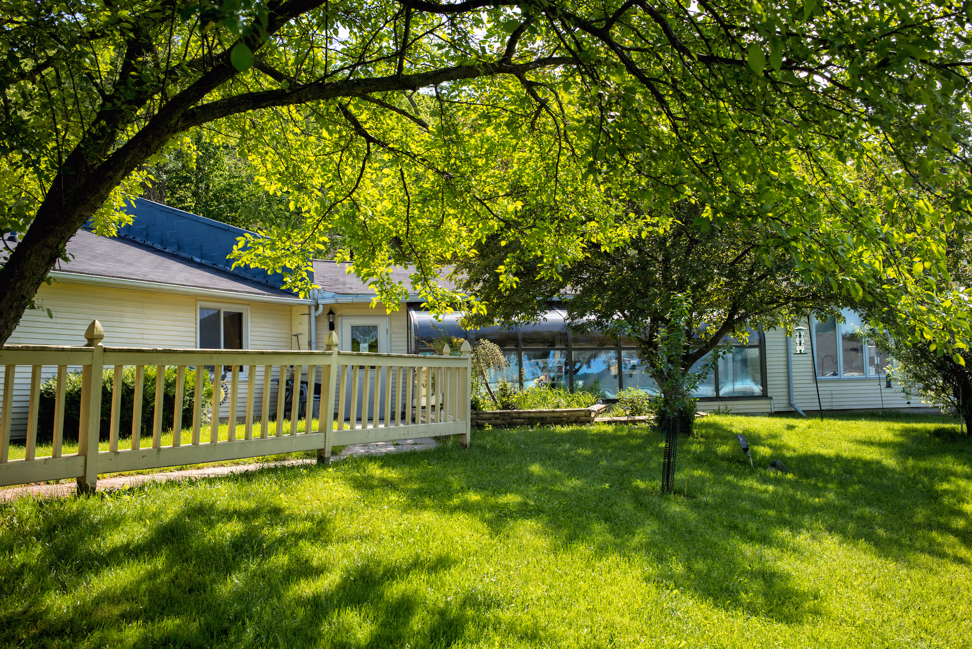 Exterior view of Harvest Guest Home with green lawn, trees, and a wooden fence.