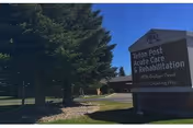 Outdoor view of the entrance area to Teton Post Acute Care & Rehabilitation facility with a sign displaying the name and address, surrounded by trees and a clear blue sky.