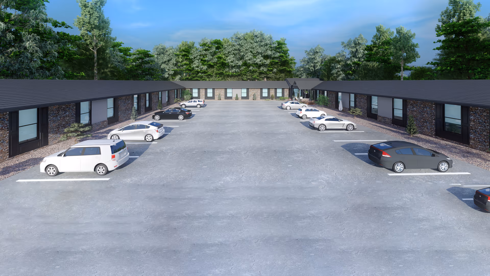 Parking lot with several parked cars surrounded by single-story buildings with stone facades and black roofs, set against a backdrop of green trees under a blue sky.