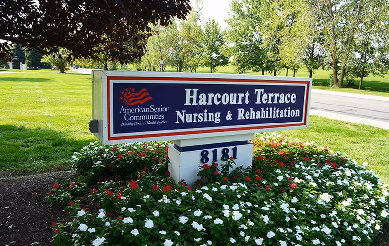 Outdoor sign for Harcourt Terrace Nursing & Rehabilitation surrounded by red and white flowers with green grass and trees in the background.