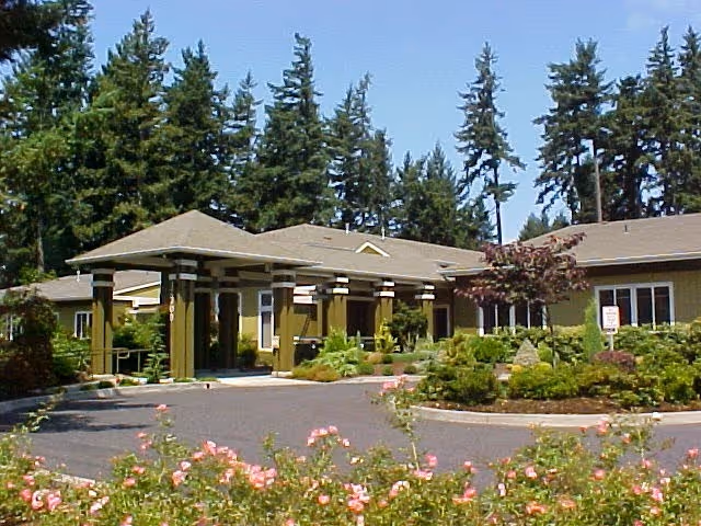 Single-story memory care building entrance with a covered porte-cochere, circular driveway and landscaped flowerbeds.
