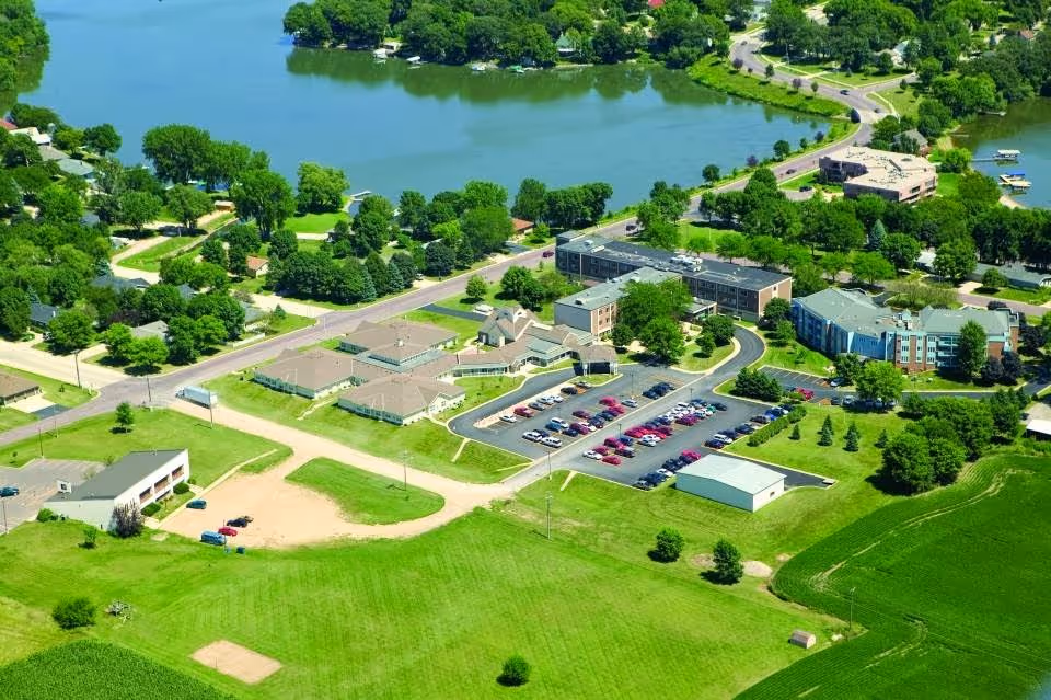 Aerial view of a lakeside health care campus with multiple buildings, parking lots, and surrounding green lawns and trees.