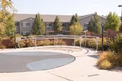 Exterior view of a two-story senior living building with landscaped courtyard, circular paved area and metal railings.