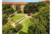 Landscaped courtyard with walkways and lawns surrounded by multi-story brick apartment buildings and trees.