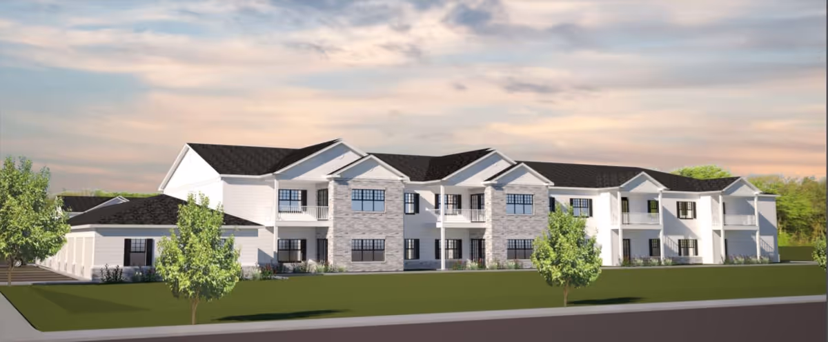 Two-story white residential building with balconies and stone accents facing a grassy lawn under a cloudy sky.