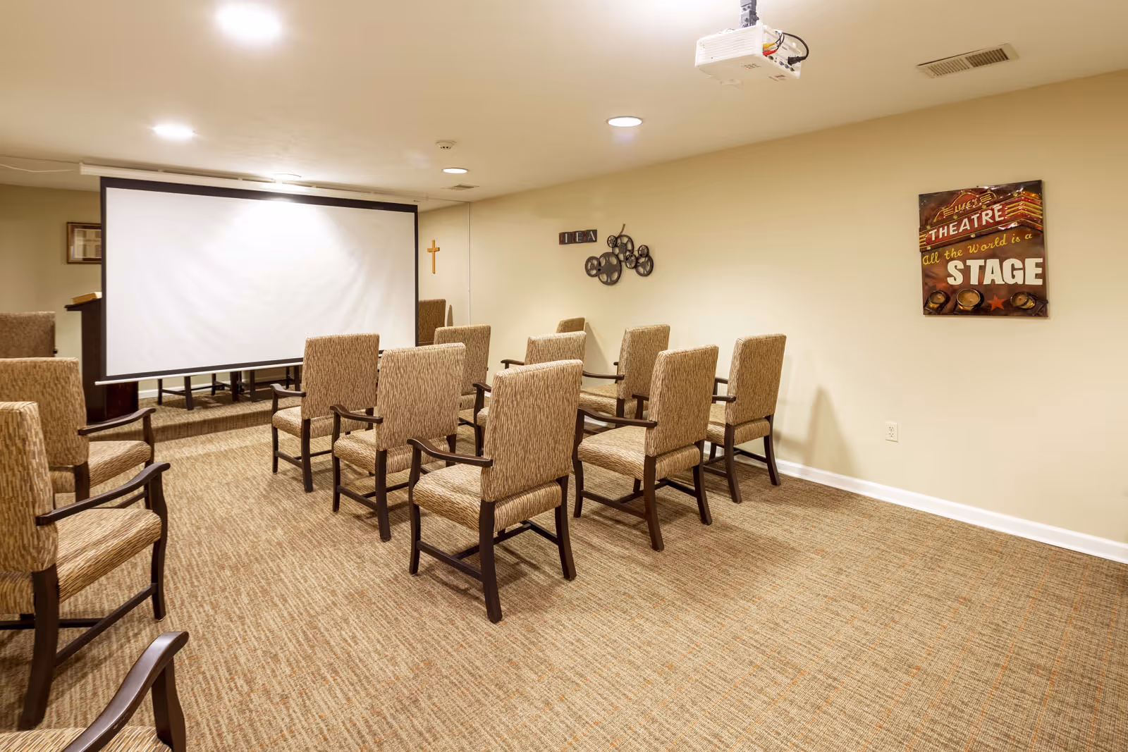 Small screening room with rows of upholstered chairs facing a projection screen and wall decor.