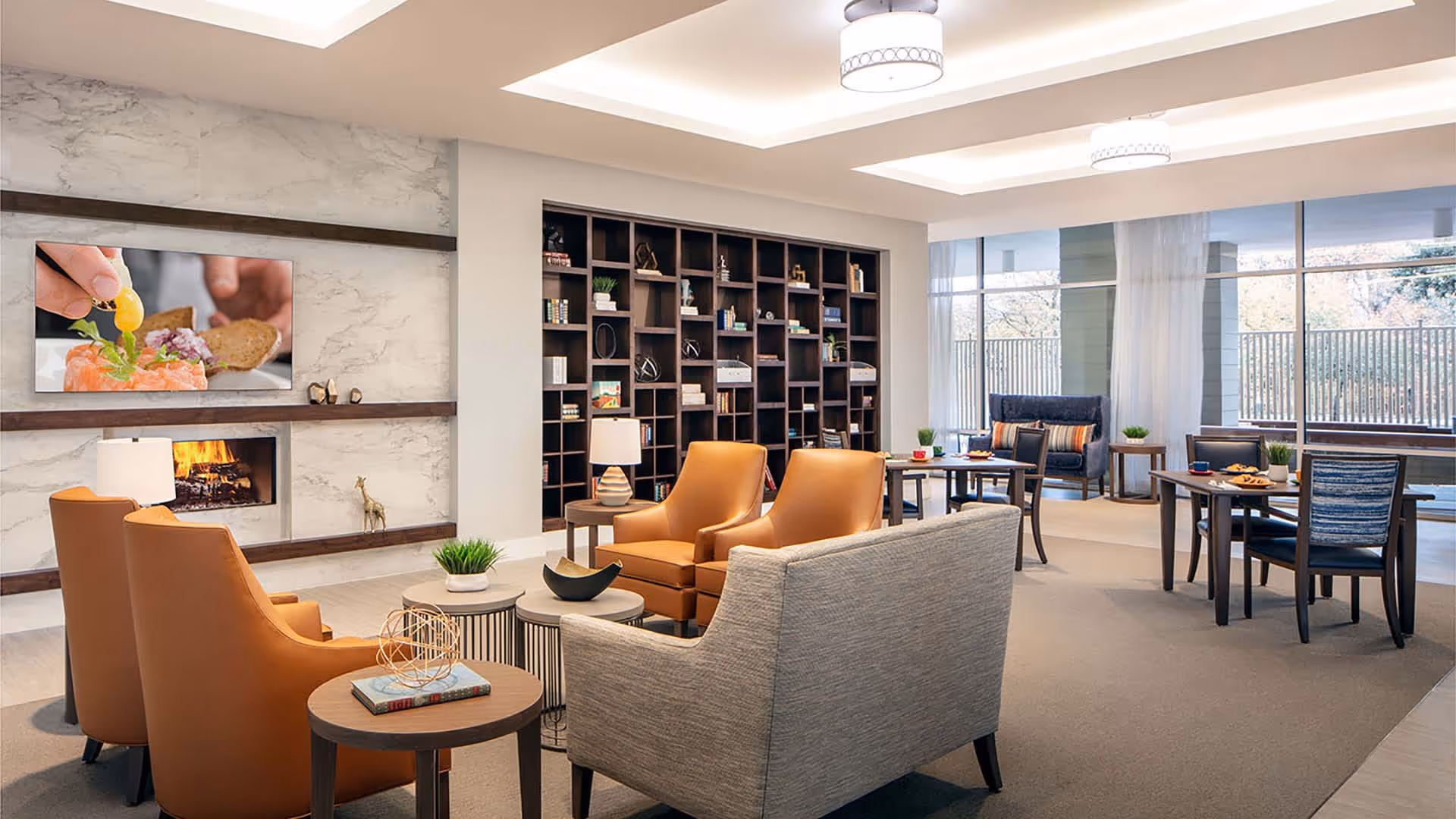 Modern senior living common room with leather armchairs, a sofa, coffee tables, built-in bookshelf, fireplace, and large windows.