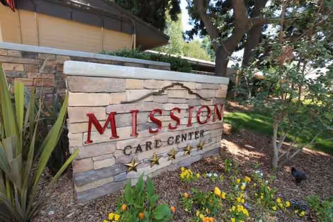 Mission Care Center sign on stone facade with flowers and trees.