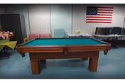 A pool table in a community room with chairs, an American flag on the wall, and a table with computers.