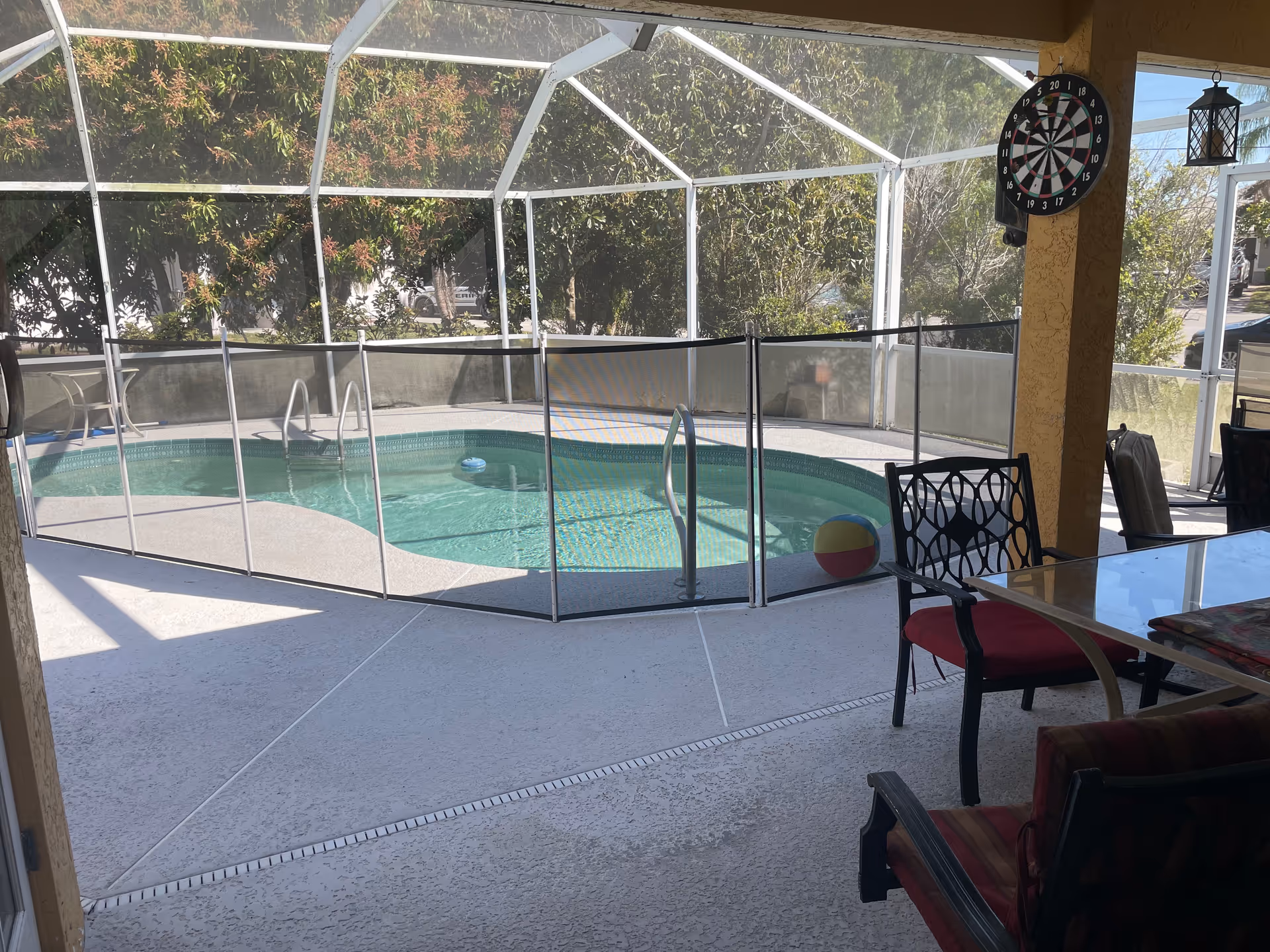 Enclosed outdoor pool area with patio dining furniture and a dartboard.