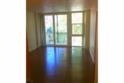 Empty room with wooden flooring and large sliding glass doors leading to a balcony with a view of trees outside.