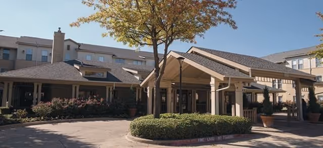 Front entrance and porte-cochère of a multi-story senior living building with landscaping and a circular drive.