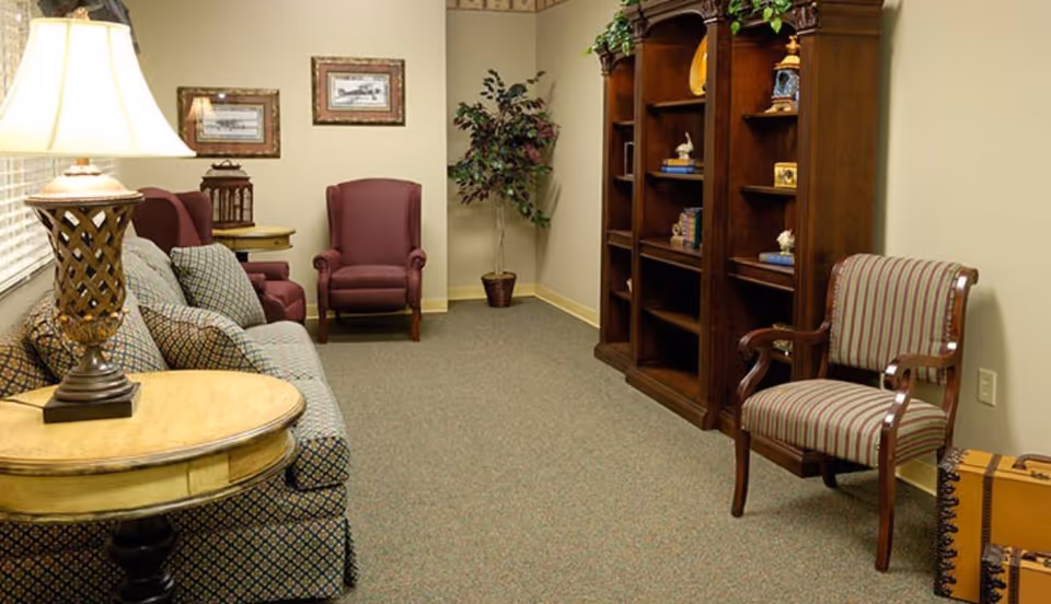 Cozy furnished sitting room with a sofa, armchairs, wooden bookshelf, side tables and a lamp.