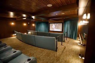 Small private movie theater with tiered teal seating facing a projection screen in a wood-paneled room.