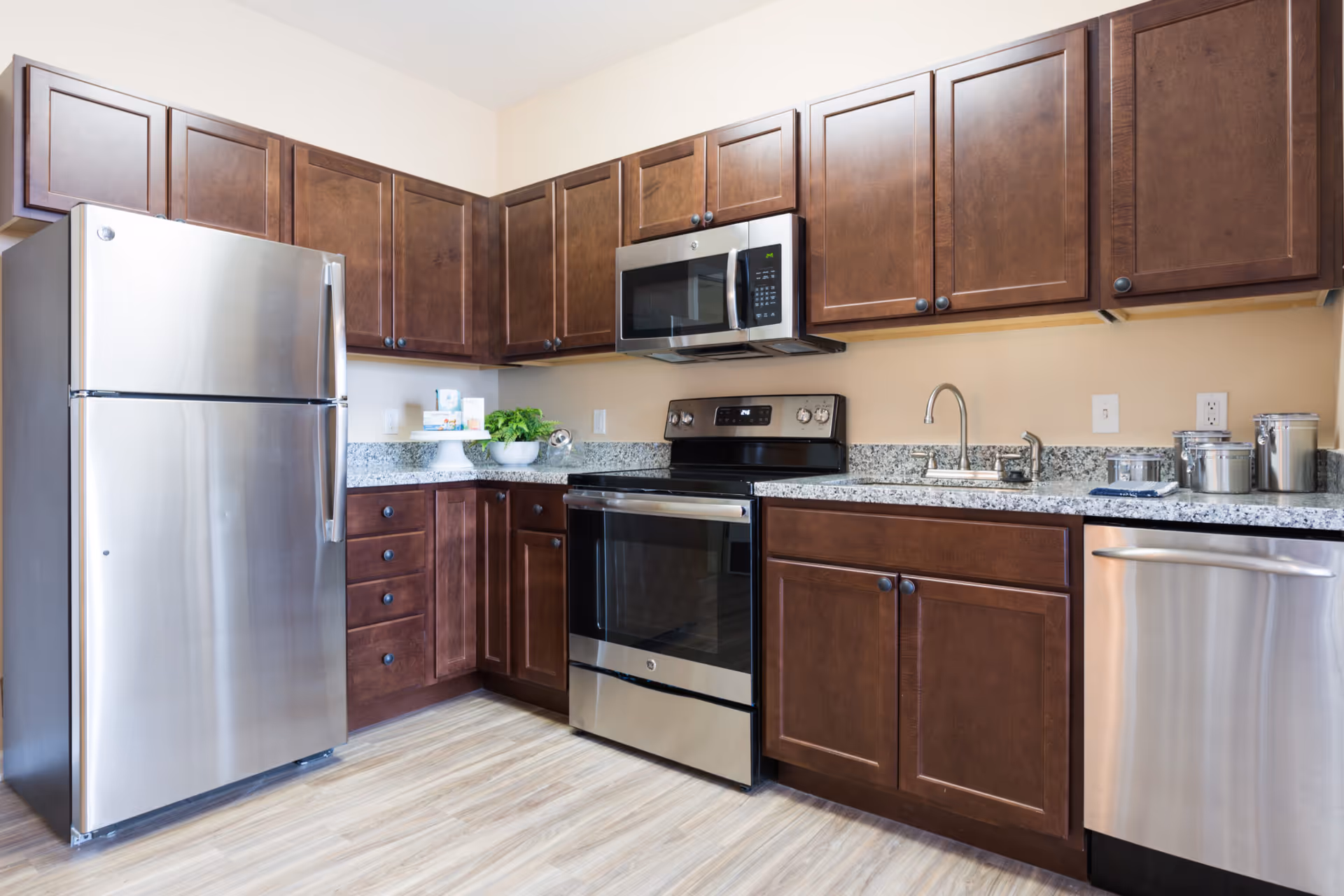 Modern kitchen with stainless steel refrigerator, oven, microwave and dishwasher, dark wood cabinets and granite countertops.