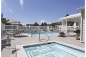 Outdoor pool and hot tub area with lounge chairs, umbrellas, and a pergola under a clear sky.