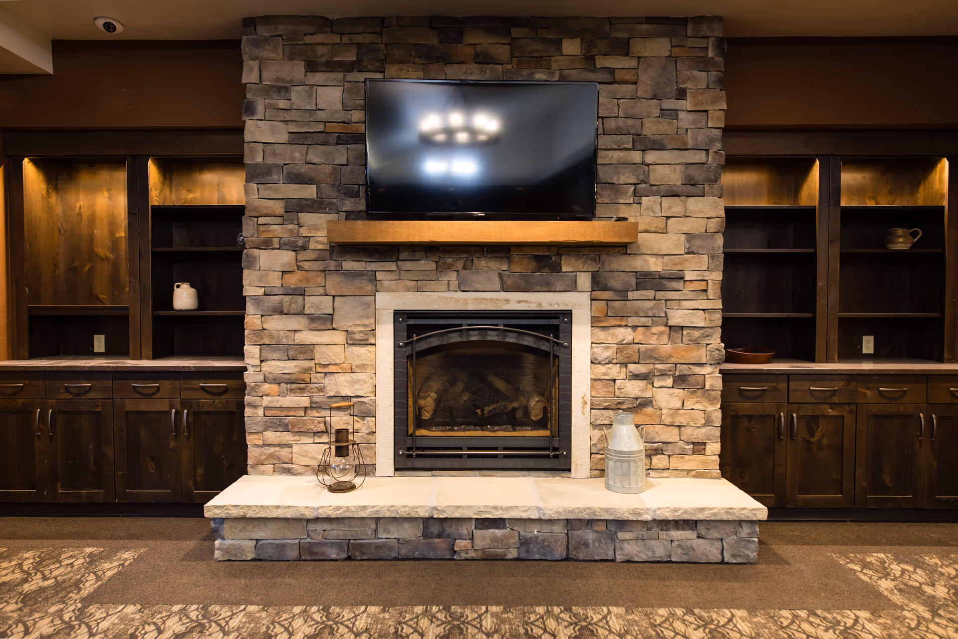 Stone fireplace with a mounted TV flanked by dark wood built-in cabinets in a cozy common room.