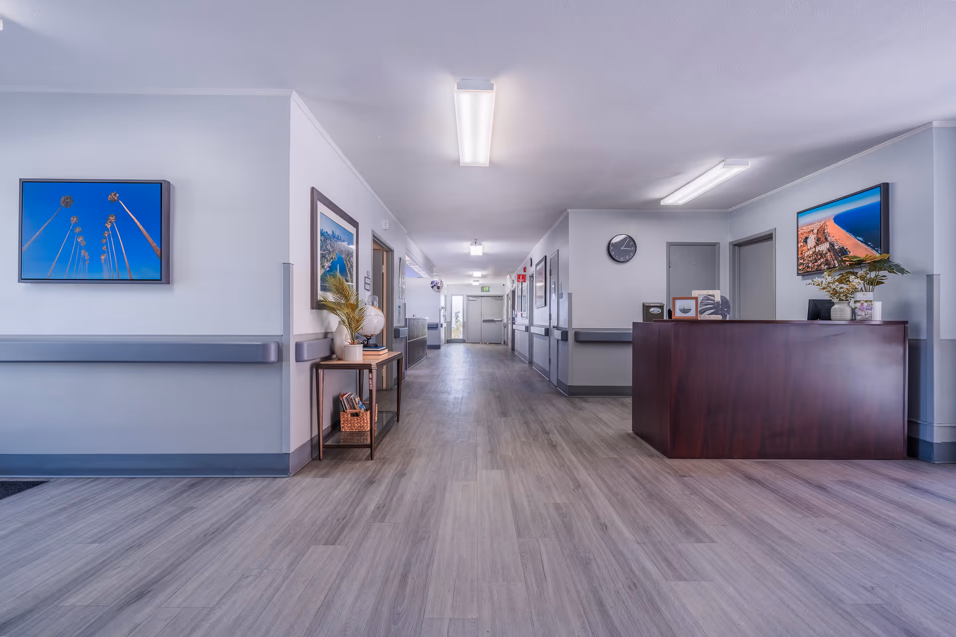 Bright, wide interior hallway and reception desk with wood-look flooring, framed artwork, and handrails.