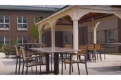 Outdoor courtyard patio with a covered gazebo and several tables and chairs in front of a multi-story building.