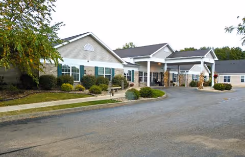 Front exterior of a single-story senior living building with a covered entrance, driveway, and landscaped shrubs.