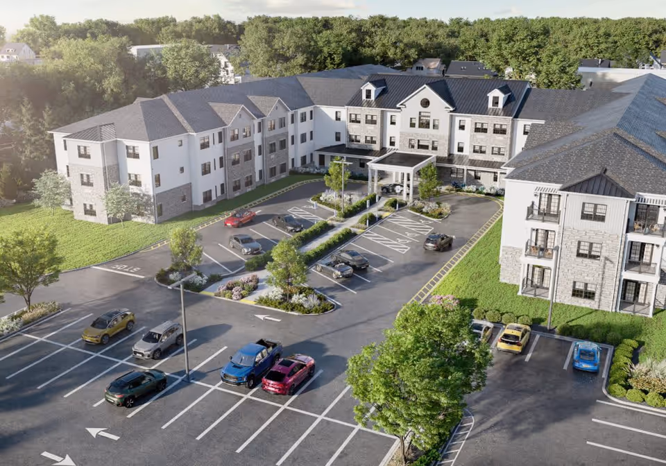 Aerial view of a senior living facility named Azalea at Cinnaminson showing a large three-story building with a covered entrance, surrounded by parking lots with several parked cars, landscaped greenery, and trees.