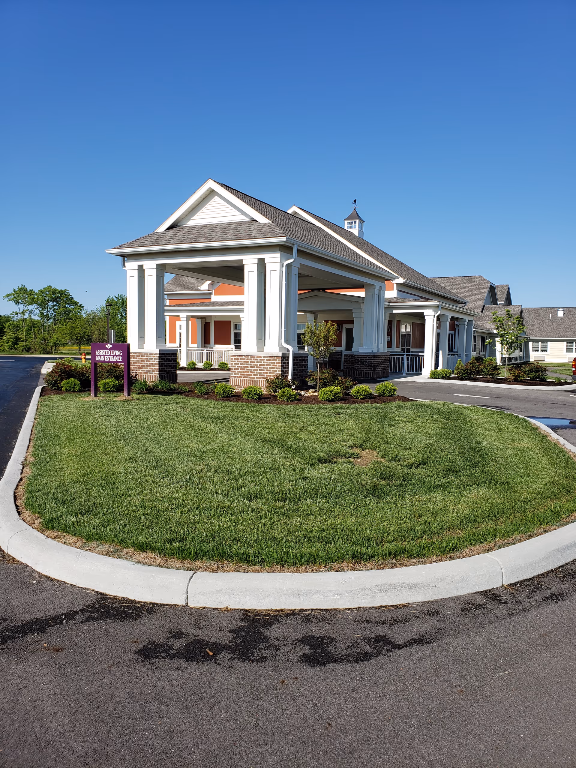 Exterior view of Court House Manor showing the main entrance with a covered driveway, landscaped lawn, and clear blue sky.