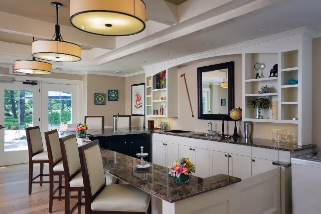 Bright communal kitchenette and bar area with marble countertops, bar stools, built-in shelving and pendant lights.