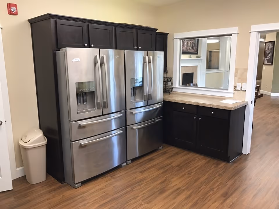 Two stainless steel French-door refrigerators flanked by dark wood cabinets and a countertop in a communal kitchen area.