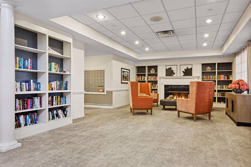 Carpeted communal lounge with built-in bookshelves, a fireplace and orange armchairs grouped around a coffee table.