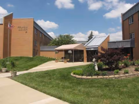 Exterior view of Pelham Manor senior living with brick buildings, walkway, and outdoor seating area.