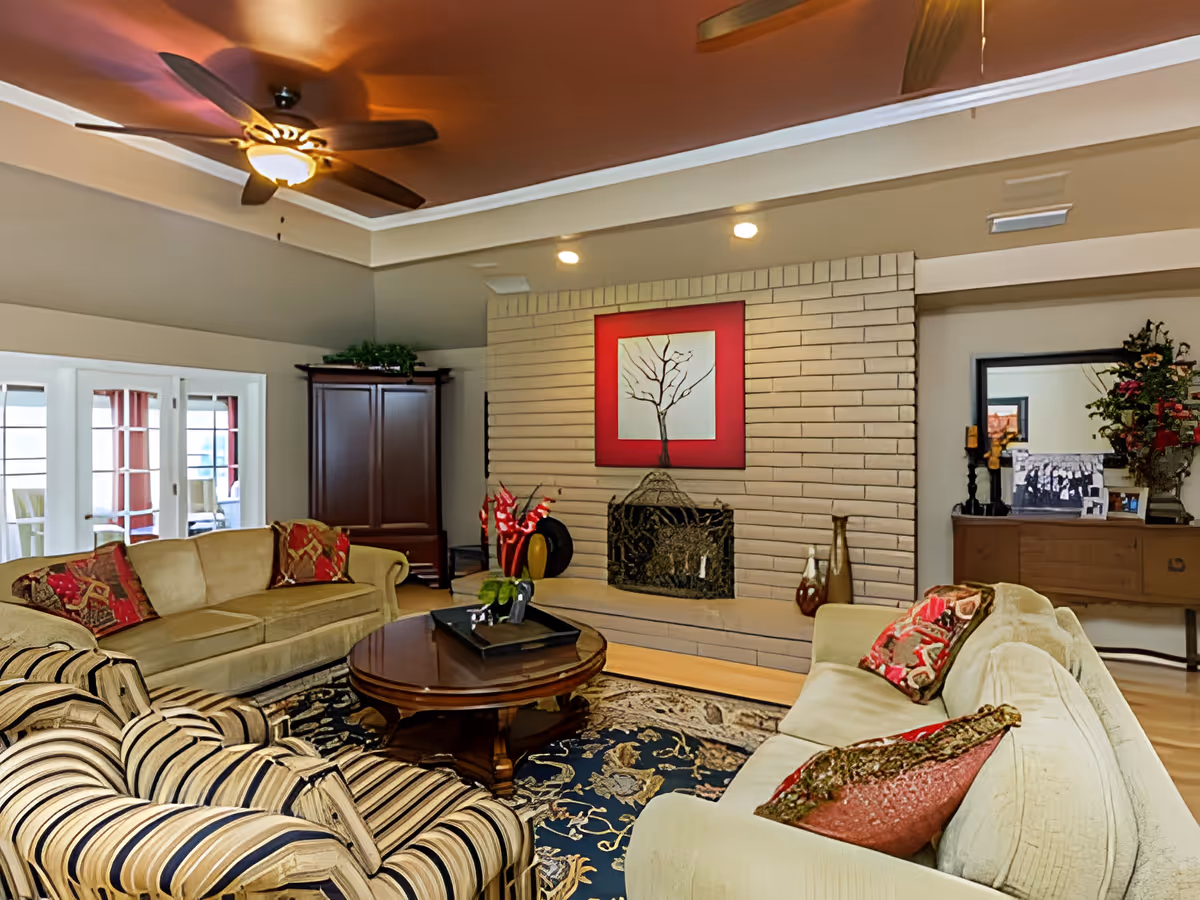Cozy living room with sofas, a striped armchair, round coffee table, and a brick fireplace topped by framed artwork.
