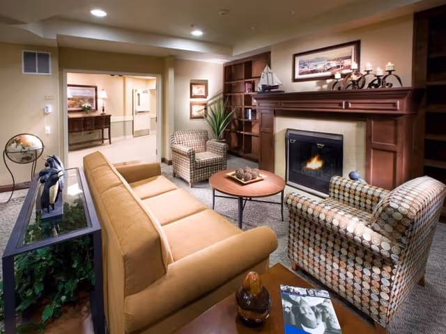 Cozy living room with a sofa, patterned armchairs, a coffee table, built-in shelving and a lit fireplace.