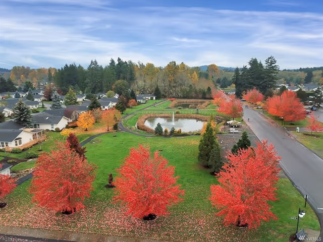 Aerial view of a landscaped community green with a central pond and fountain surrounded by homes and bright red autumn trees.