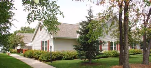 Single-story facility with a well-kept lawn, trees, and a sidewalk pathway.